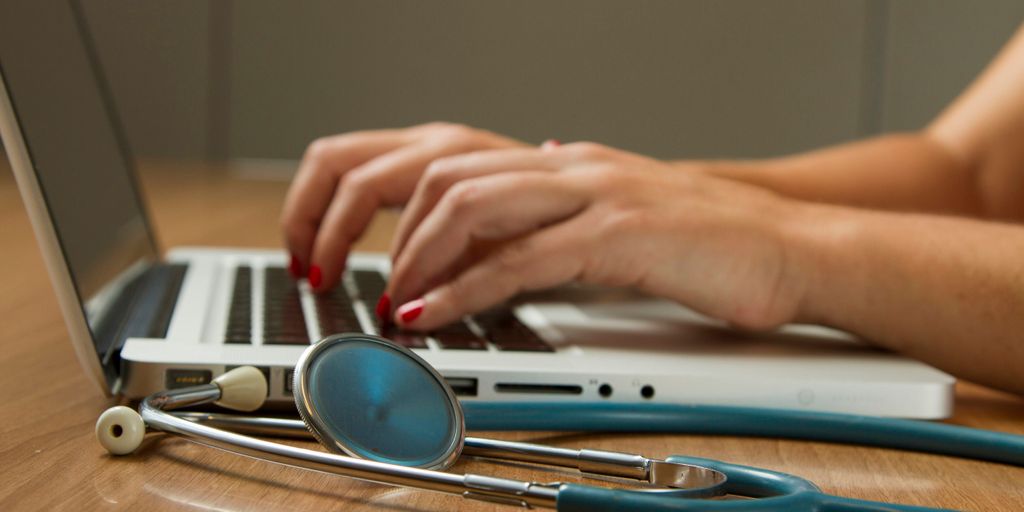 person sitting while using laptop computer and green stethoscope near