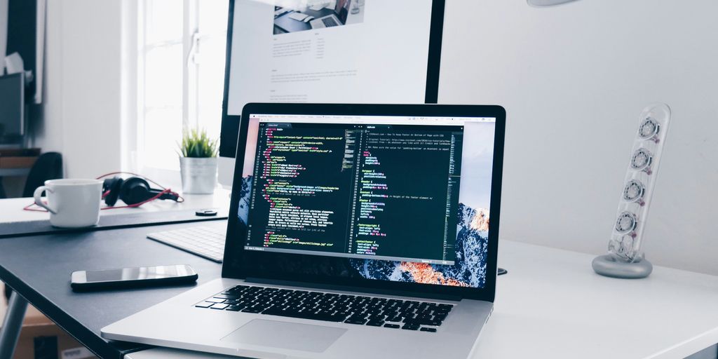 A MacBook with lines of code on its screen on a busy desk